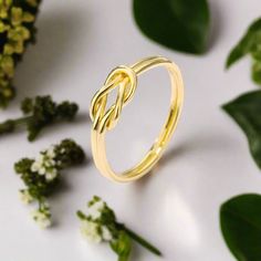 a gold ring sitting on top of a white surface next to flowers and greenery