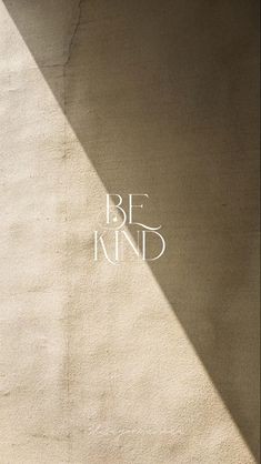 the words be kind are written in white on a beige stucco wall with a shadow