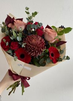 a bouquet of red flowers and greenery in someone's hand with white background