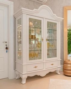 a white china cabinet with glass doors and gold trimmings in a living room