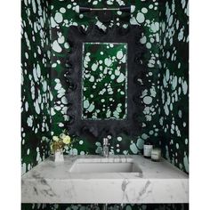 a white sink sitting under a mirror in a green wallpapered bathroom with black and white decor