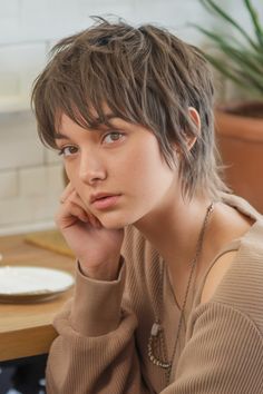 Young person with short, textured hair, gazing thoughtfully while resting their chin on their hand. Shagged Bob Haircut, Short Pixie Shag Haircut, Short Shag For Fine Hair, Women Shag Haircuts, Short Edgy Shag Haircut, Short Shag Haircuts For Fine Hair, Shag Wolf Cut Short, Pixie Cut With Fringe, Short Alternative Haircuts