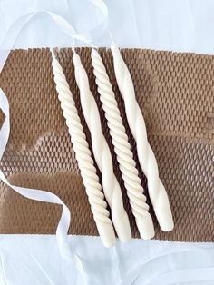 three white candles sitting on top of a brown paper bag next to a white ribbon