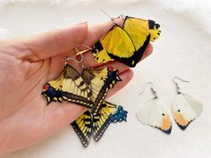 a hand holding three butterfly shaped earrings in it's left hand next to another pair of earrings