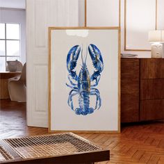 a blue and yellow lobster is displayed in front of a white framed art print on a wooden floor