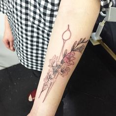 a woman with a flower tattoo on her arm holding a scissors in one hand and flowers in the other