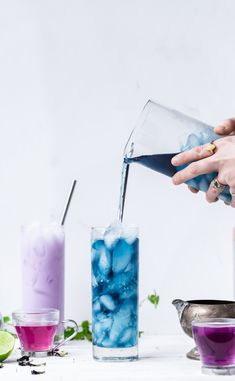 a person pouring blue liquid into a glass filled with ice and limes next to other drinks