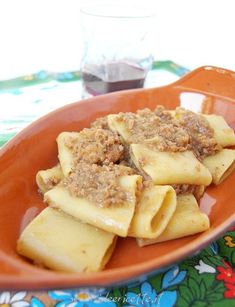 pasta with meat and sauce in an orange bowl on a floral table cloth next to a glass of wine