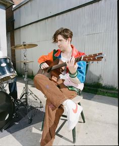 a man sitting on a chair playing an acoustic guitar in front of a drum set