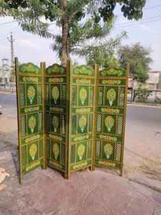 an ornately painted wooden room divider next to a tree on the side of a road