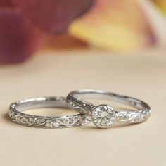 two wedding rings sitting on top of a table with flowers in the background and one ring has a diamond