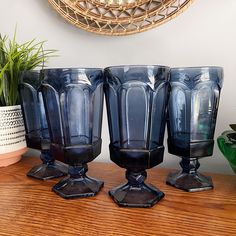 three blue glass vases sitting on top of a wooden table next to a potted plant