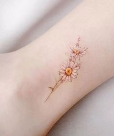 a small flower tattoo on the left side of the leg, with an orange center