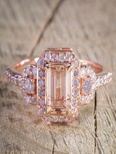 a fancy ring with an emerald surrounded by white and pink diamonds on a piece of wood