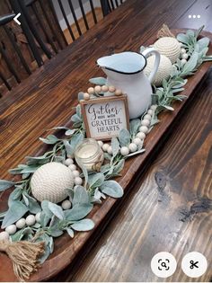 a wooden table topped with a white pitcher and greenery