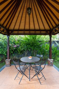 a table and chairs under an umbrella in a backyard area with plants on the other side