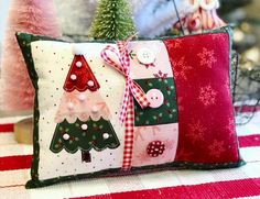 two decorative christmas pillows on top of a red and white striped tablecloth with small trees