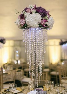 a tall centerpiece with purple and white flowers on the top is adorned with crystal beads