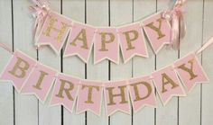 a pink and gold happy birthday banner hanging on a wall next to a wooden fence