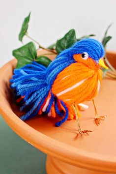 a small blue and orange bird sitting on top of an orange bowl with green leaves