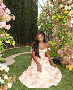 a woman in a floral dress sitting on the ground next to some pink and yellow flowers