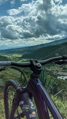 a mountain bike parked on top of a grass covered hillside under a cloudy blue sky