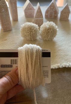 someone is holding yarn in front of small white houses on a table with other knitted items