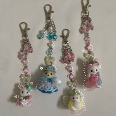 four key chains with various charms attached to them on a white surface, one is holding a teddy bear and the other has a stuffed animal