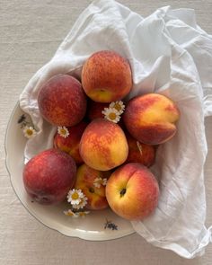 a bowl filled with lots of ripe peaches on top of a white table cloth