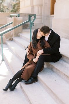 a man and woman sitting on the steps kissing each other while they are dressed in black