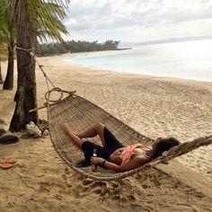 a woman laying in a hammock on the beach