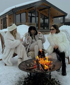 three women sitting around a fire pit in the snow drinking wine and having a conversation