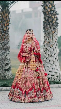 a woman in a red and gold bridal gown standing next to two palm trees