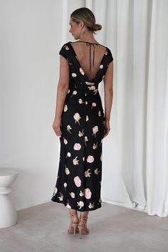 a woman standing in front of a white wall wearing a black dress with pink flowers on it