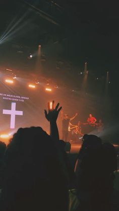 a person raising their hand up in front of a crowd at a concert with lights on