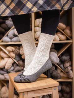 a woman's legs with socks and shoes on top of a stool in front of some balls of yarn