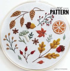 an embroidery pattern with leaves, mushrooms and oranges on white fabric in a hoop