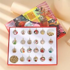 a box with twelve christmas ornaments hanging from it's sides and a book in the background