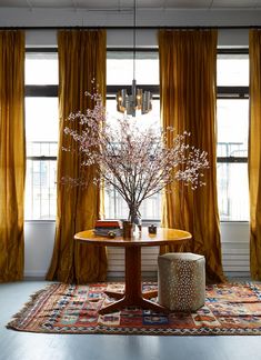 a dining room table with a vase on top of it next to yellow drapes