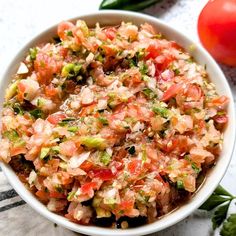 a white bowl filled with lots of food next to a tomato