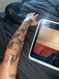 a person's arm with flowers on it next to a mirror and a laptop