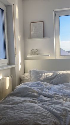 an unmade bed with white sheets and pillows in front of two windows overlooking the ocean