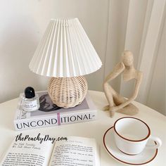 a table with a lamp, coffee cup and book on it next to an open book