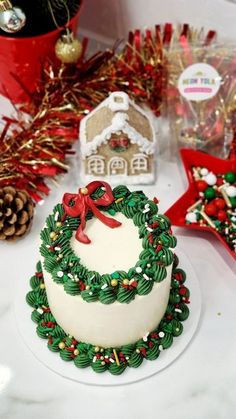 a white cake with green and red decorations on it sitting next to other christmas items