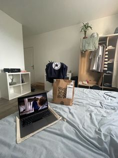 an open laptop computer sitting on top of a bed next to a cardboard bag and clothes