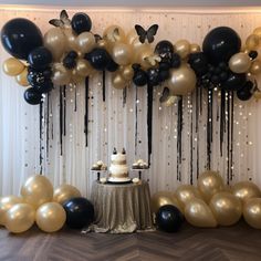 a table topped with a cake surrounded by black and white balloons on top of a wooden floor