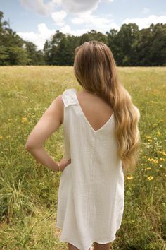 This is a white sleeveless v neck dress with a ruffle detail on the shoulder. The model is wearing a size small