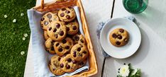 chocolate chip cookies in a wicker basket next to a glass of water on a picnic table