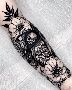 a black and white tattoo on the arm with flowers, leaves and a skull in it