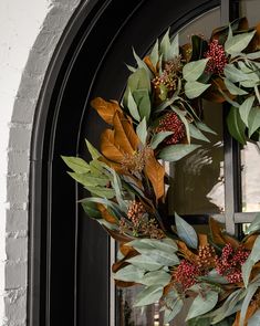 a wreath on the front door of a house with leaves and berries hanging from it